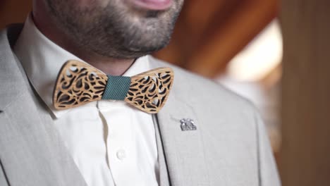 Groom-in-gray-suit-and-with-stubble-adjusting-wooden-bow-tie,-close-up