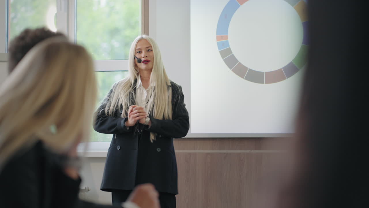 En energisk kvinne taler på en forretningskonferanse, hvor hun som ekspert demonstrerer diagrammer og forklarer.
