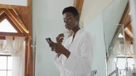 Mujer-Atractiva-Afroamericana-Cepillándose-Los-Dientes-Y-Usando-Un-Teléfono-Inteligente-En-El-Baño.