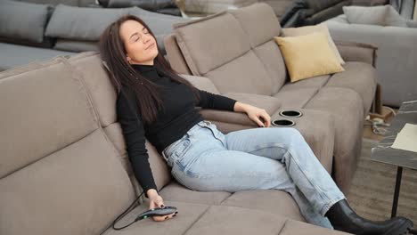 a woman is testing a modern sofa in a furniture store using the remote control for the massage a woman tests a modern sofa in a furniture store using a remote control to check functions such as massage