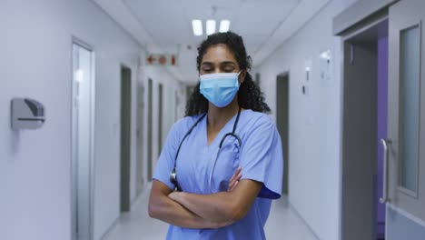 Portrait-of-asian-female-doctor-wearing-face-mask-and-scrubs-standing-in-hospital-corridor