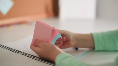 Little-girl-flips-sticky-papers-in-pack-sitting-at-desk