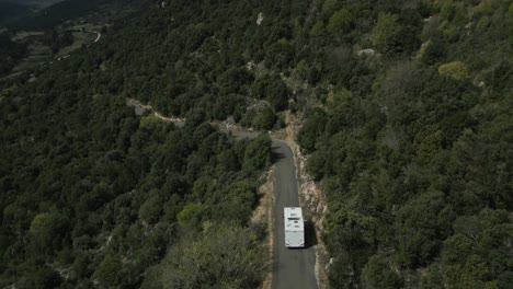 Large-white-motorhome-is-driven-along-a-narrow-road-in-the-countryside