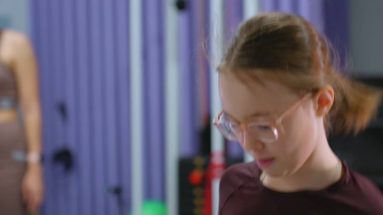 primer plano de un niño con gafas saltando enérgicamente durante la sesión de entrenamiento, el fondo borroso presenta la actividad de monitoreo del instructor de gimnasia mientras otro niño está en el suelo