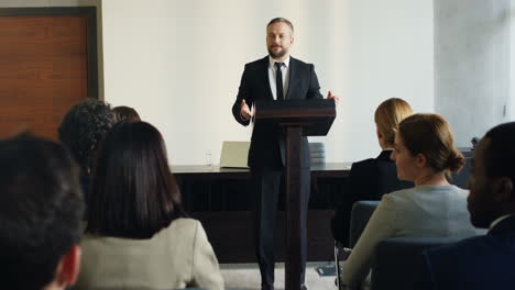 caucasian mature businessman wearing formal clothes speaking at a conference in front of many people