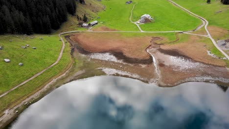 Sobrevuelo-Aéreo-Sobre-Seealpsee-En-Appenzell,-Suiza-Con-Movimiento-Inverso-Y-Panoramización-Revelando-Un-Reflejo-De-Los-Picos-Alpstein-En-El-Lago