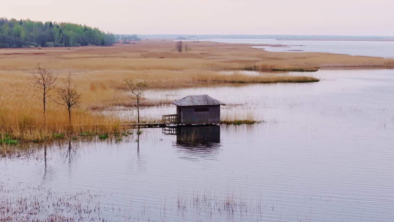 Friedliche Seeszene zeigt eine hölzerne Vogelbeobachtungshütte zwischen Schilf und ruhigen Wasserspiegelungen.