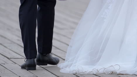 close-up of a groom's feet, stepping on a wooden boardwalk, trailing bride's dress