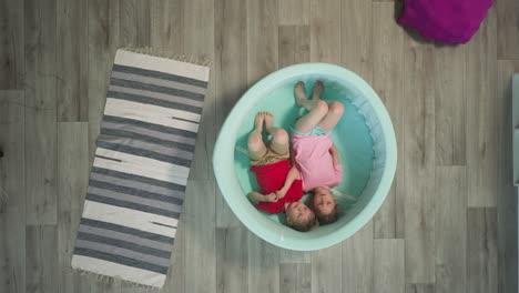 Brother-and-sister-lie-in-shallow-pool-near-rug-on-floor