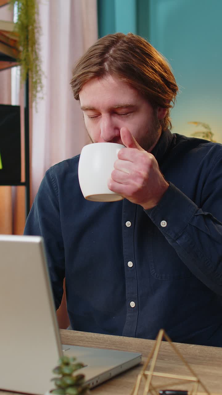 Forretningsmand, der arbejder på bærbar computer, drikker en kop varm kaffe og sidder ved et bord på hjemmekontoret