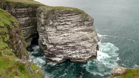 Breathtaking-view-of-a-sea-cliff-and-the-great-sea-stack-of-Handa-Island-covered-in-a-bustling-seabird-colony-full-of-breeding-populations-of-puffins-guillemots,-kittiwake-and-razorbills-in-Scotland