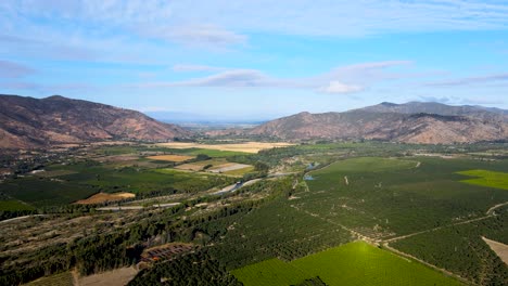 aerial panning of green farm field surrounded by mountains on a cloudy day, cachapoal valley, south of santiago, chile