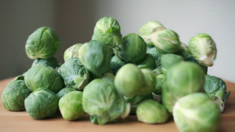 Brussels-Sprouts-Falling-In-Slow-Motion-onto-Heap-on-Light-Wood-Cutting-Board,-Slight-Push-In-Movement