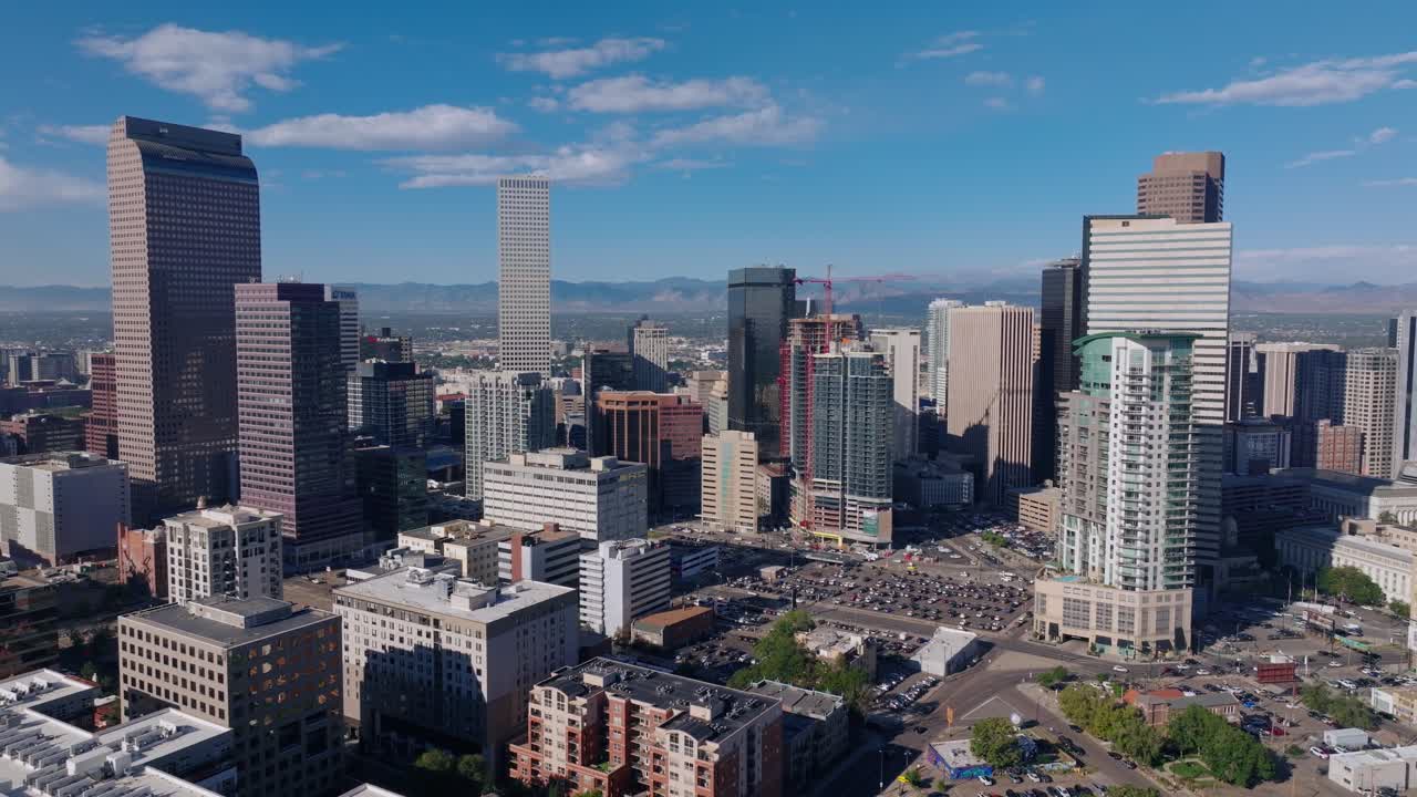 Panoramica aerea dello skyline del centro di Denver sotto la luminosa luce di mezzogiorno, con un ampio pullback mentre le auto scorrono sotto.