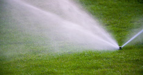 medium shot of grass sprinkler splashes water over the lawn 6