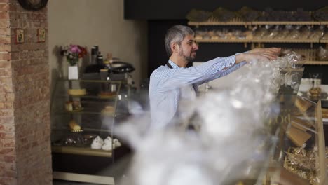 Close-up-handsome-salesman-putting-cookies-on-the-counter-in-bakery-store