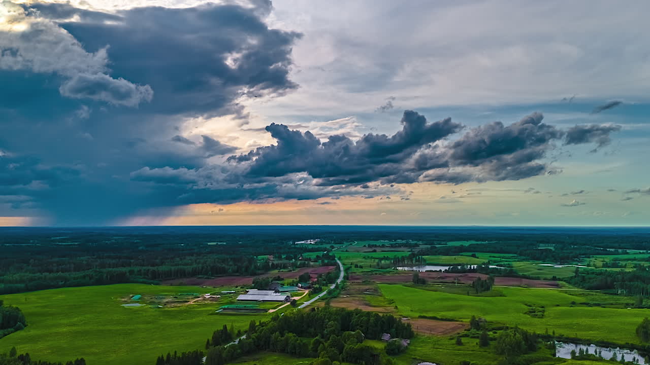 Cloudscape and rain is swept along an idyllic countryside, farms, and forests at sunset - high altitude aerial time lapse