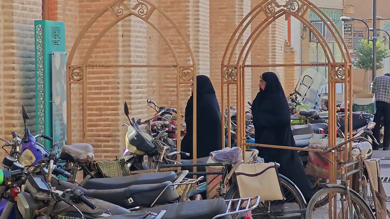 Due donne in chador che camminano davanti a motociclette parcheggiate in Iran