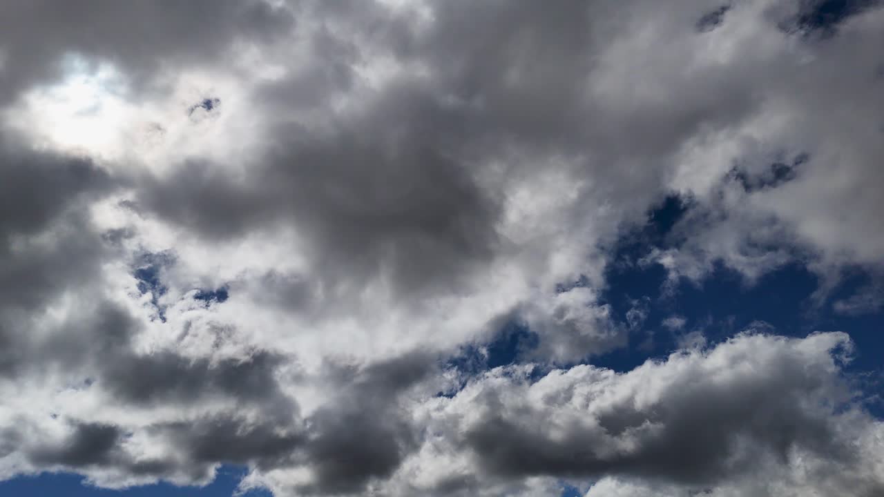 Dense cumulus clouds drift rapidly across a deep blue sky in a daylight timelapse, creating dynamic lighting and a moody, atmospheric effect