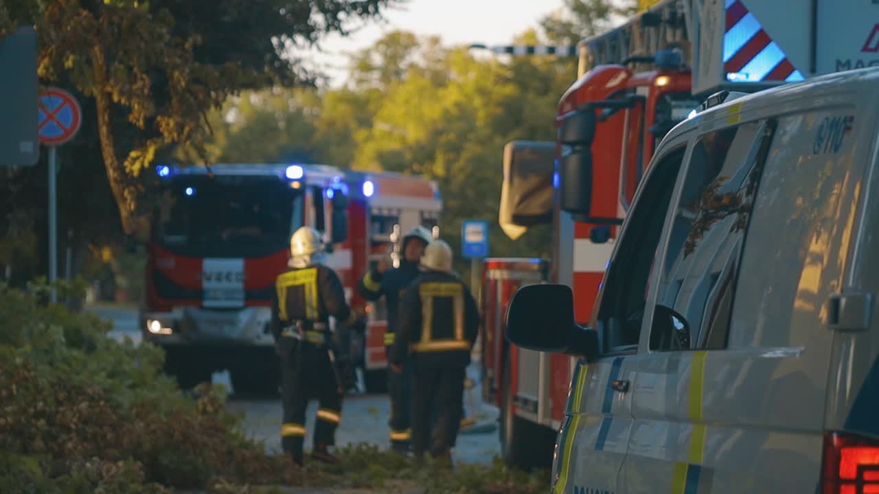 A police car with activated beacon lights is parked on a town road at night. Surrounding buildings and streetlights are visible, creating a calm urban atmosphere. Copy space available.