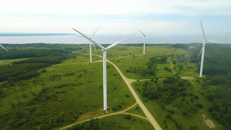 aerial drone footage panning in front and revealing large white wind turbines where their blades are rotating and spinning creating electical renewable green energy on a cloudy peninsula, sea shore