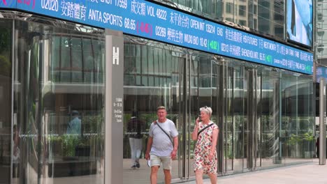 hong kong stock exchange: people walking past stock ticker