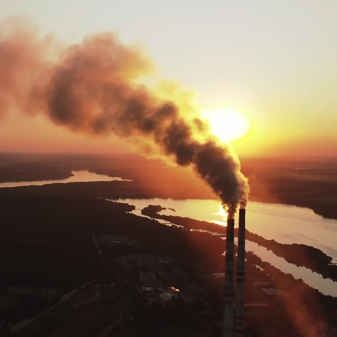 Pipes pollute atmosphere with smoke against the setting sun. Ecology pollution. Smoke stacks emit from industry on the background of lakes at sunset