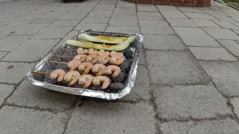 Locked-off-view-of-disposable-mini-BBQ-grill-with-Zucchini-and-Shrimp-skewers
