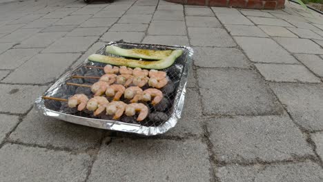 locked off view of disposable mini bbq grill with zucchini and shrimp skewers