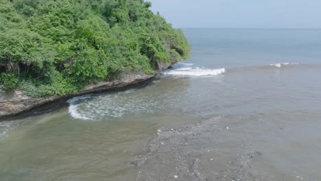 Low-altitude-aerial-drone-shot-over-polluted-muddy-sewage-water-and-floating-trash-with-debris-over-dead-coral-reef-mixing-with-turquoise-water-and-tropical-coastine-in-Bali-Indonesia