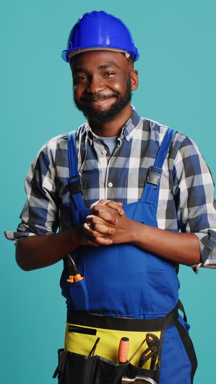 Vertical video: Young male contractor standing over blue background