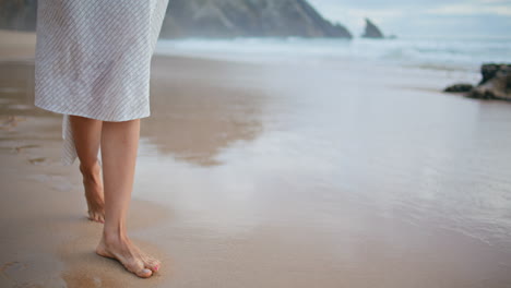 woman legs leaving footprints at ocean shore closeup. carefree girl walking sand