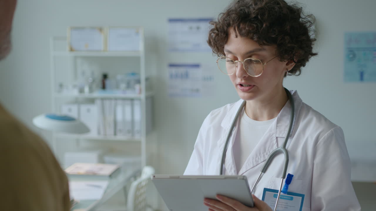 Female Doctor Using Tablet and Giving Consultation to Patient in Clinic