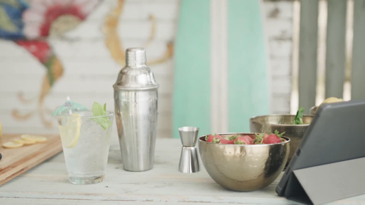 batidor de cócteles, tableta, bebidas e ingredientes en el mostrador en un bar de la playa, cámara lenta