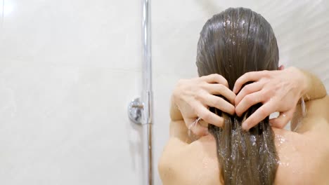 attractive young blonde woman washing her hair in the shower. rear view.