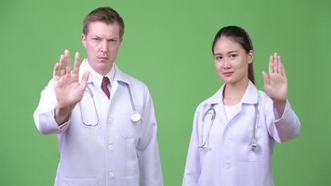 multi-ethnic couple doctors showing stop gesture together