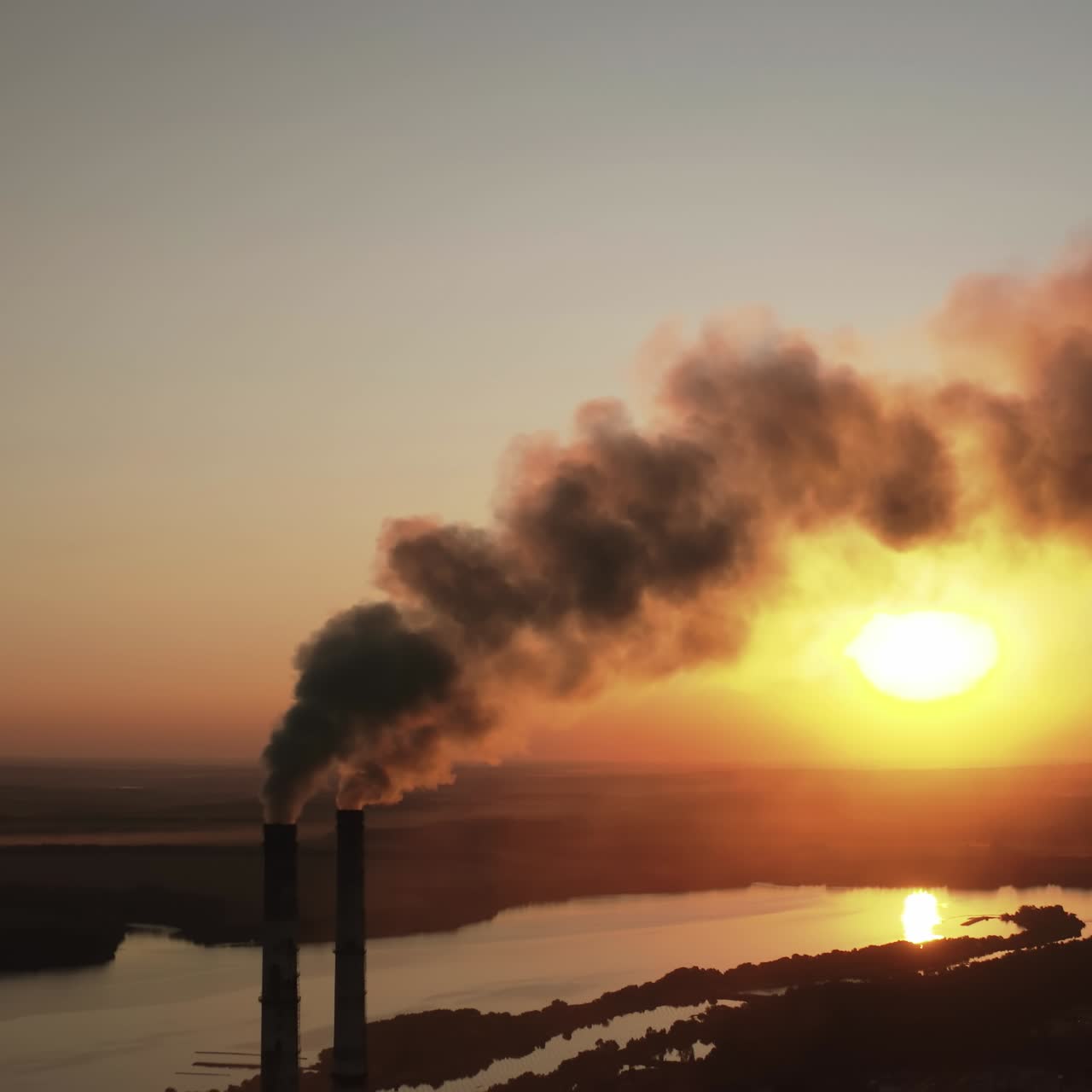 Factory pollutes environment at sunset. Toxic enterprise chimneys tubing against the evening sky background release black smoke. Smoking pipes of harmful manufacture in nature