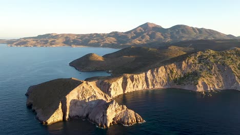 aerial drone shot of greek peninsula during golden hour sunrise or sunset with dramatic cliffs as a centerpiece