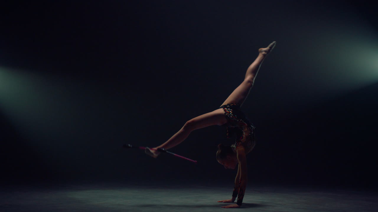 una chica delgada lanzando mazas en el espacio oscuro, una mujer deportiva haciendo salto mortal en el interior.