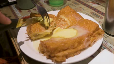 a customer cuts into small pieces a ready-to-eat hong kong style french toast consisting of deep-fried bread, peanut butter, butter, and condensed milk at a restaurant