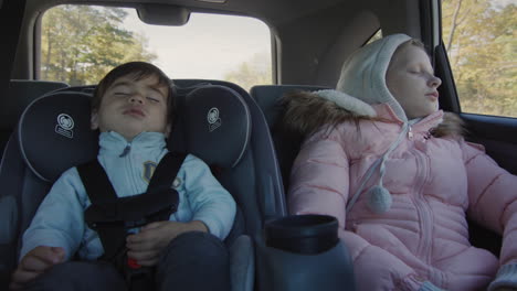 los niños que duermen conducen en el asiento trasero del coche. un bebé asiático duerme en un asiento para niños, una chica duerme a su lado.