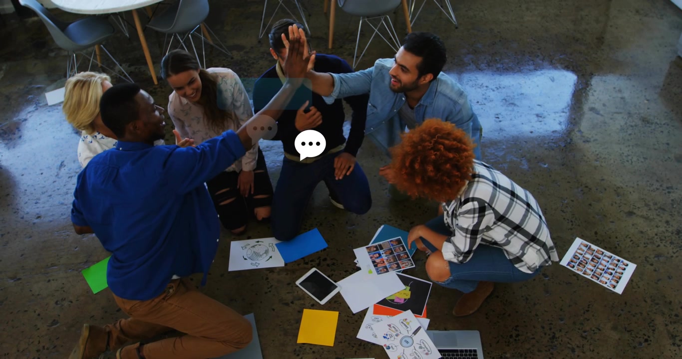 Team inginocchiato attorno a grafici e campioni di design che si danno il cinque, mentre bolle animate salgono durante un brainstorming.