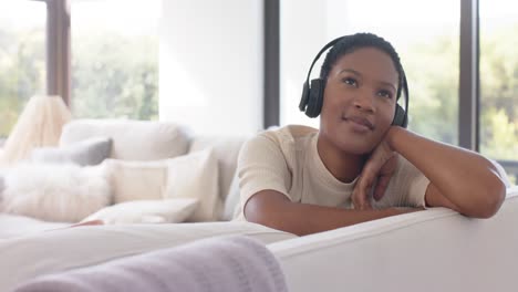 Fröhliche-Afroamerikanische-Frau,-Die-Mit-Kopfhörern-Auf-Dem-Sofa-Sitzt-Und-Musik-Hört,-Zeitlupe