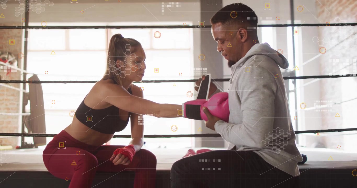 Boxer extending left gloved fist, trainer removing pink glove and adjusting red wrap in boxing ring
