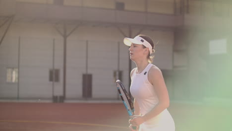 Cheerful-athlete-waiting-for-tennis-ball.-Skillful-female-tennis-player-is-preparing-to-beat-a-ball.-She-is-holding-a-racket-and-posing.-Woman-is-standing-on-tennis