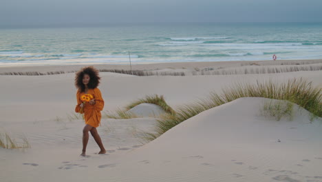 una mujer caminando por la playa al crepúsculo con flores de naranja. una chica con un ramo en la orilla del mar.