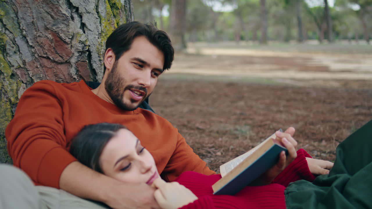 Coppia adorabile sdraiata al parco con un libro, primo piano. Uomo che legge ad alta voce per una donna tranquilla.