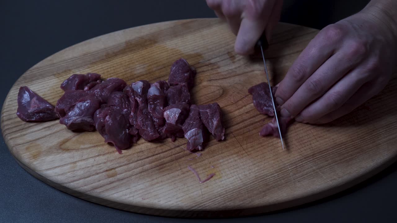 Pria mengiris daging sapi segar di atas talenan kayu - Close-up.