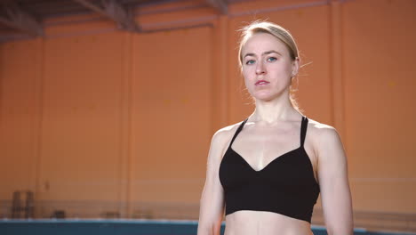 zoom in camera shot van een blonde sportvrouw die in een overdekte sportfaciliteit staat en naar de camera kijkt