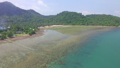 Toma-Aérea-De-La-Costa-De-La-Isla-Tropical-Con-Arrecifes-Y-Pequeños-Bungalows-En-La-Orilla